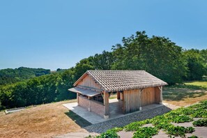 Une cabane en bois avec un toit en tuiles, une terrasse couverte et un espace recouvert de gravier agrémenté de plantes.
