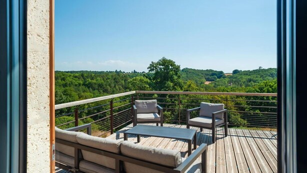 Un balcon offrant une vue sur un paysage boisé, une terrasse en bois et du mobilier d’extérieur.