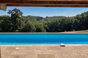 Une piscine avec vue sur une colline boisée.
