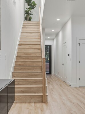 Eine Treppe mit Holzdielen und Geländer führt zu einer Zwischenebene mit einer Tür und einer Pflanze.