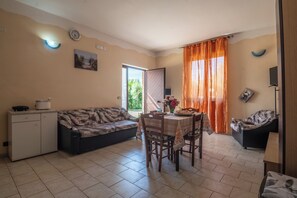 Un espai habitable reduït amb sofà, taula de dinar, cadires, un petit armari i una porta corredissa que dona a una zona exterior.