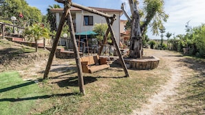 Eine rustikale Holzschaukel in einem Garten, im Hintergrund ein Haus.