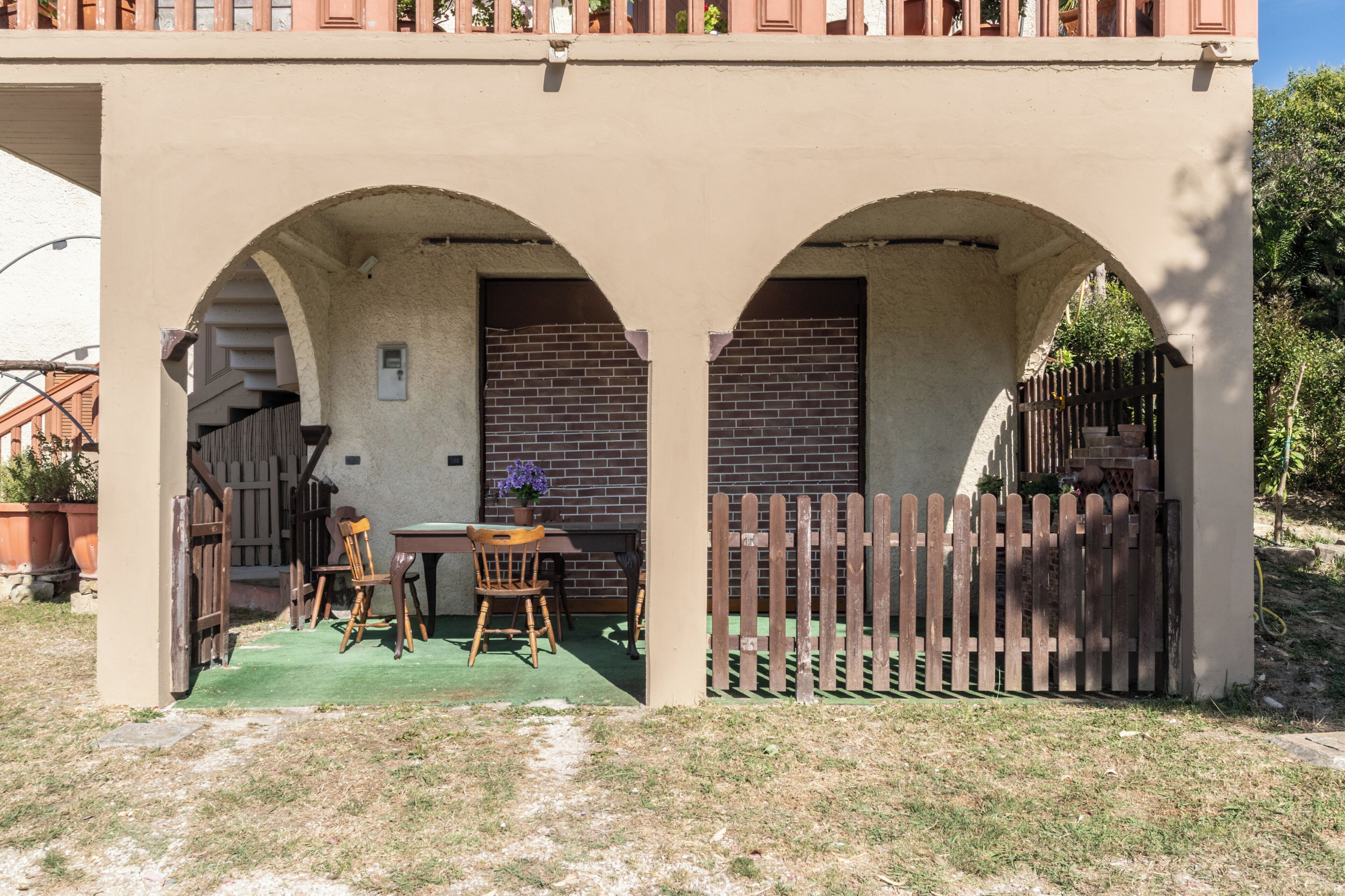 A covered outdoor seating area with a table and chairs, a brick wall, and a wooden fence.