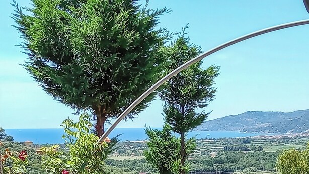 Ein Balkon mit Blumentöpfen, Blick auf das Meer und eine gebirgige Landschaft.