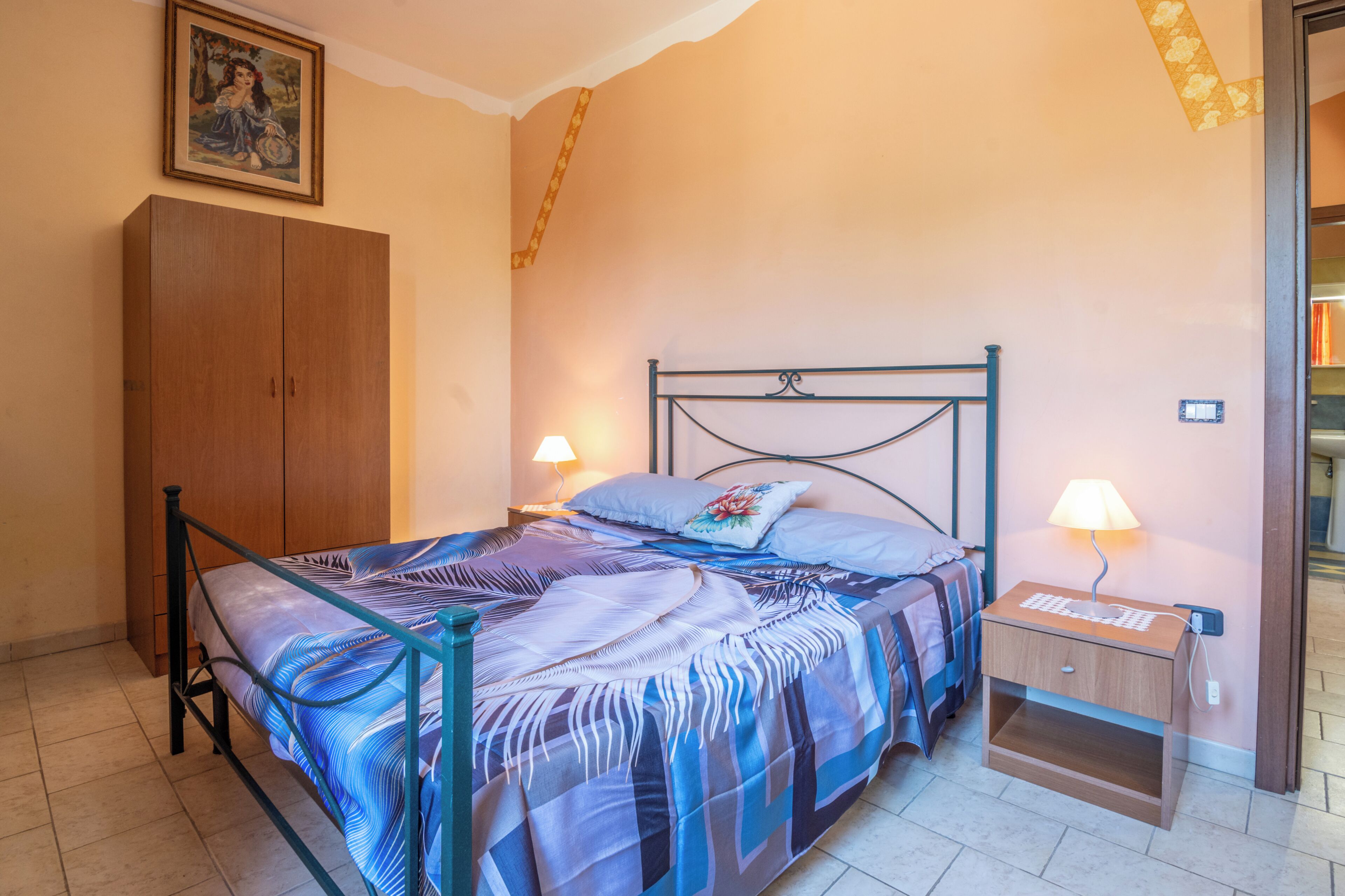 Ein Schlafzimmer mit Bett, Nachttisch, Lampe, Kleiderschrank und einem Bild an der Wand.