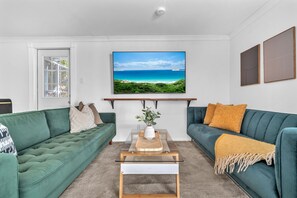 Ein Wohnzimmer mit einem grünen Sofa, einem Couchtisch und einem Fernseher, der eine Strandansicht zeigt.