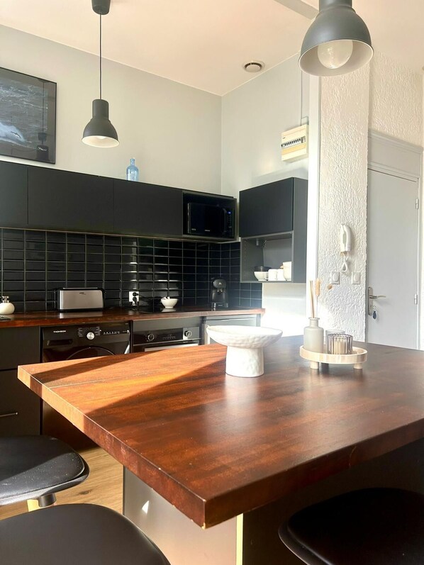 A modern kitchen with a wooden island, black appliances, and a white textured wall. - Arcachon, Right in the Heart of Downtown—Bright, New York-Style (Arcachon)