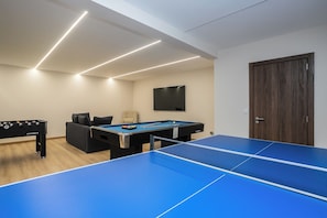 A room with a blue ping pong table, a pool table, and a foosball table.