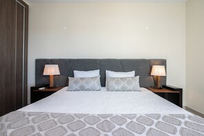 A neatly made bed with a patterned bedspread, two bedside lamps, and a dark headboard.