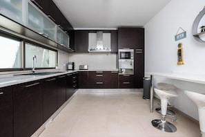 A modern kitchen with dark cabinetry, stainless steel appliances, and a white bar stool.