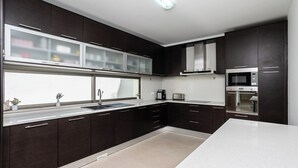 A modern kitchen with dark cabinetry, a white countertop, and stainless steel appliances including a microwave and oven. - Villa Miradouro Do Sul by Marenssa (Moncarapacho)