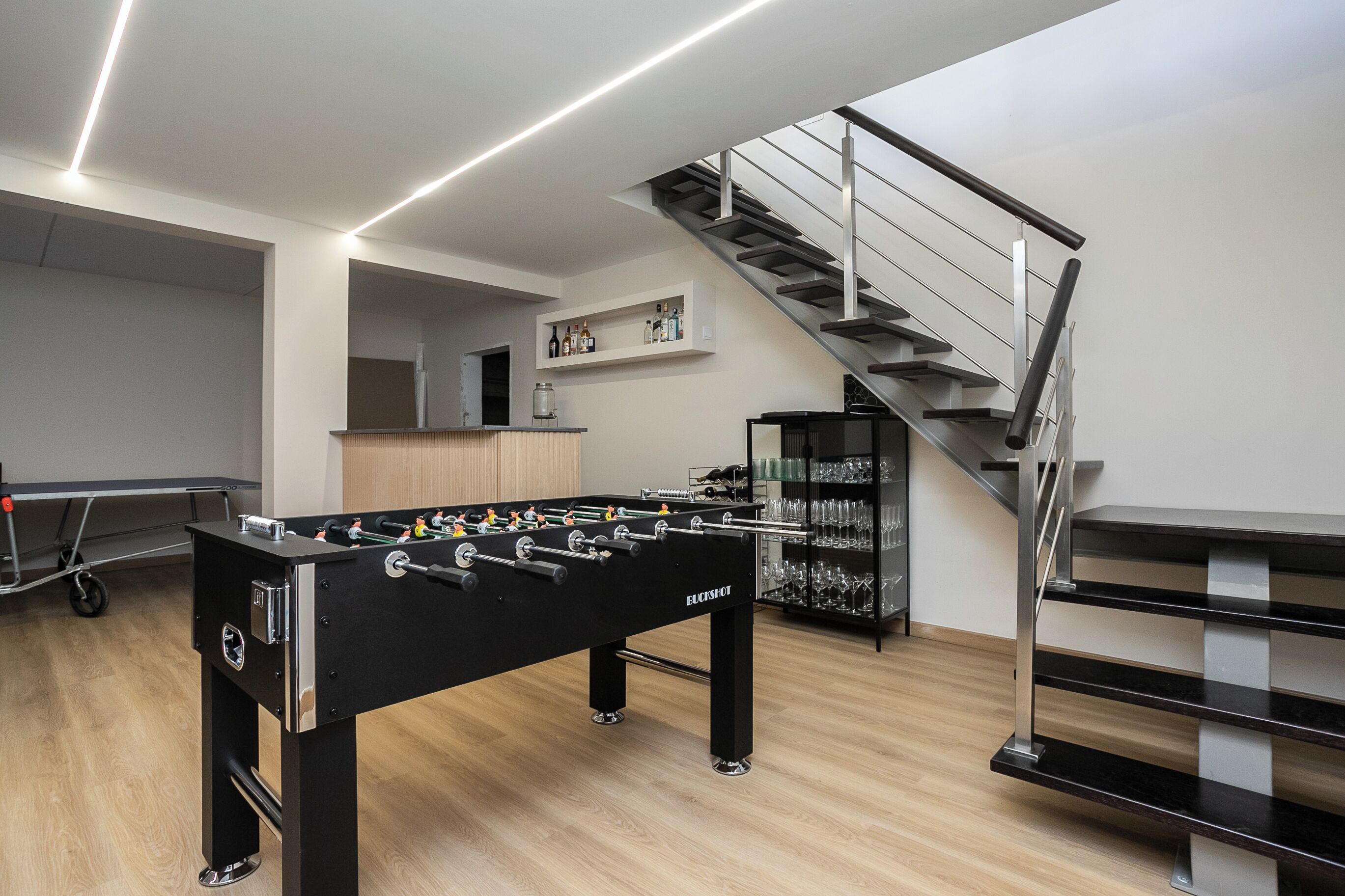 A modern indoor space with a foosball table, a staircase, and a bar area.
