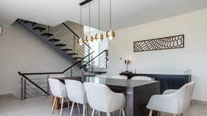 A modern kitchen with a central island, white chairs, and a staircase. - Villa Miradouro Do Sul by Marenssa (Moncarapacho)