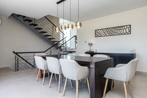 A modern kitchen with a central island, white chairs, and a staircase. - Villa Miradouro Do Sul by Marenssa (Moncarapacho)