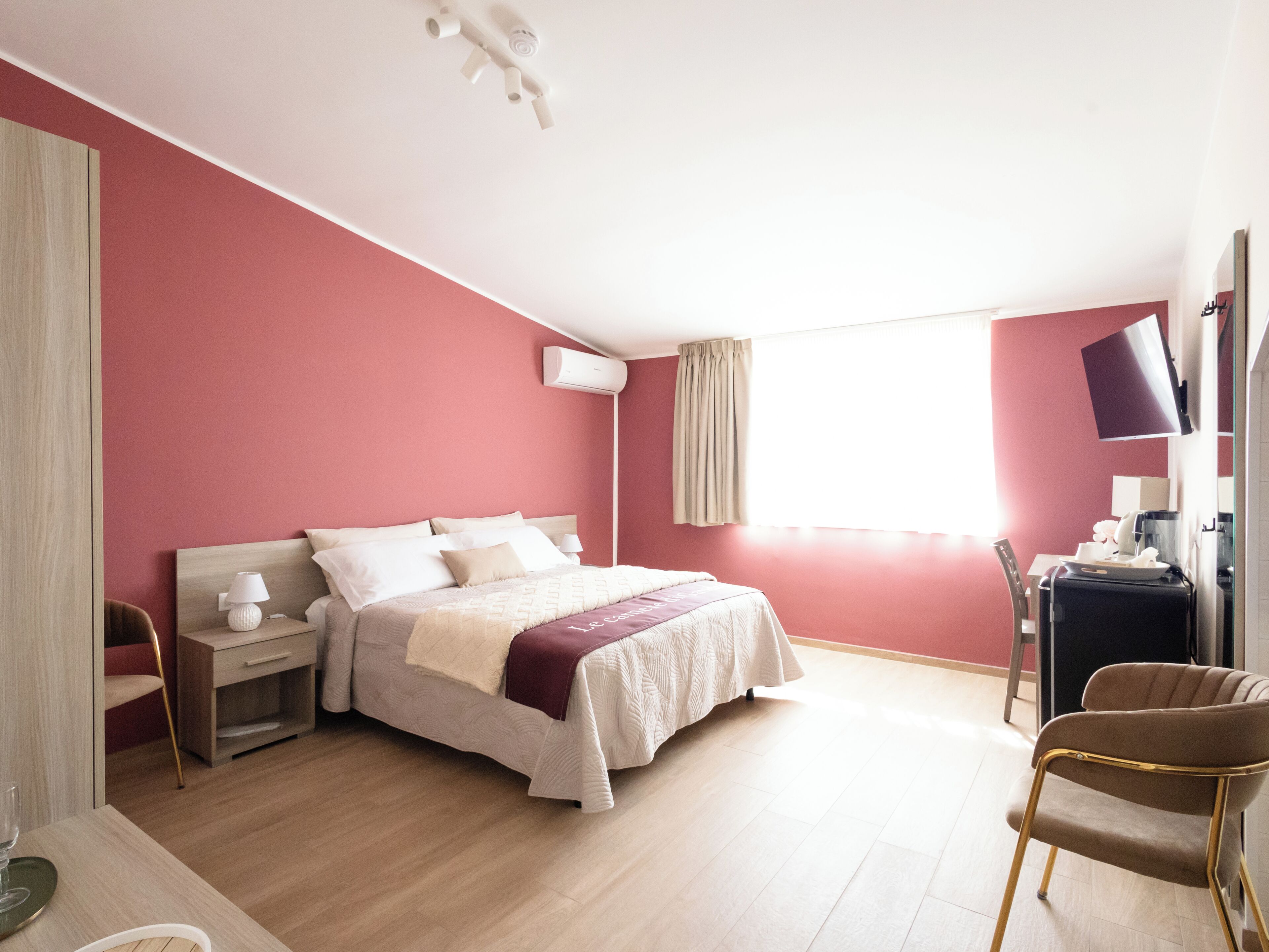A bedroom with a bed, bedside tables, a chair, a desk with a computer, and a window.