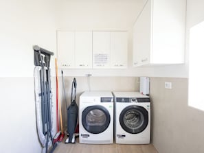 Une buanderie Ă©quipĂ©e de deux machines Ă laver, dâun aspirateur et de planches Ă repasser.