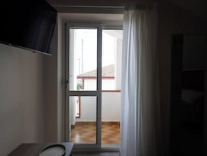 Une piĂšce dotĂ©e dâune porte-fenĂȘtre coulissante donnant sur un balcon dont le toit est recouvert de tuiles.