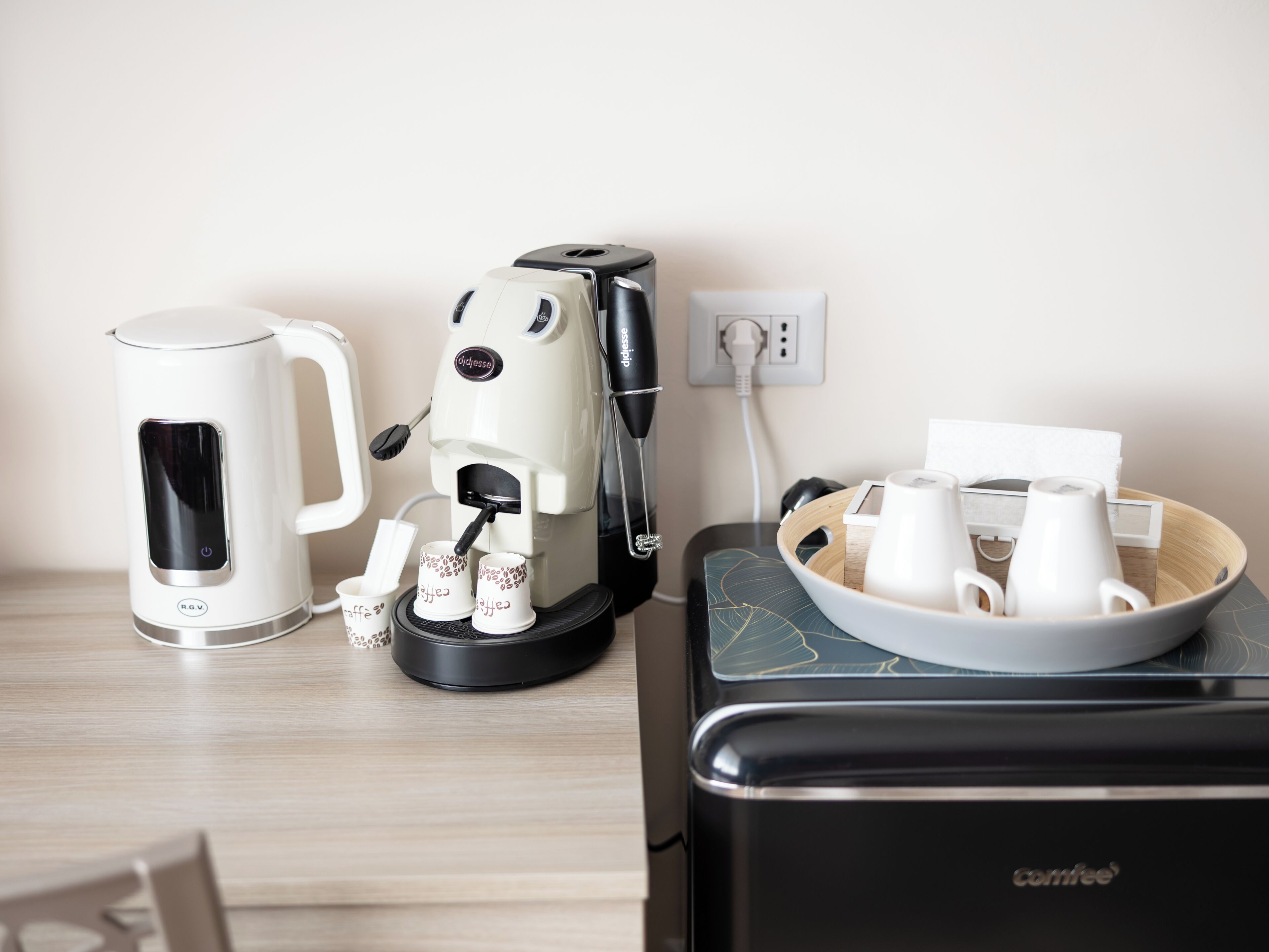A coffee maker, a kettle, and a coffee cup holder on a table.