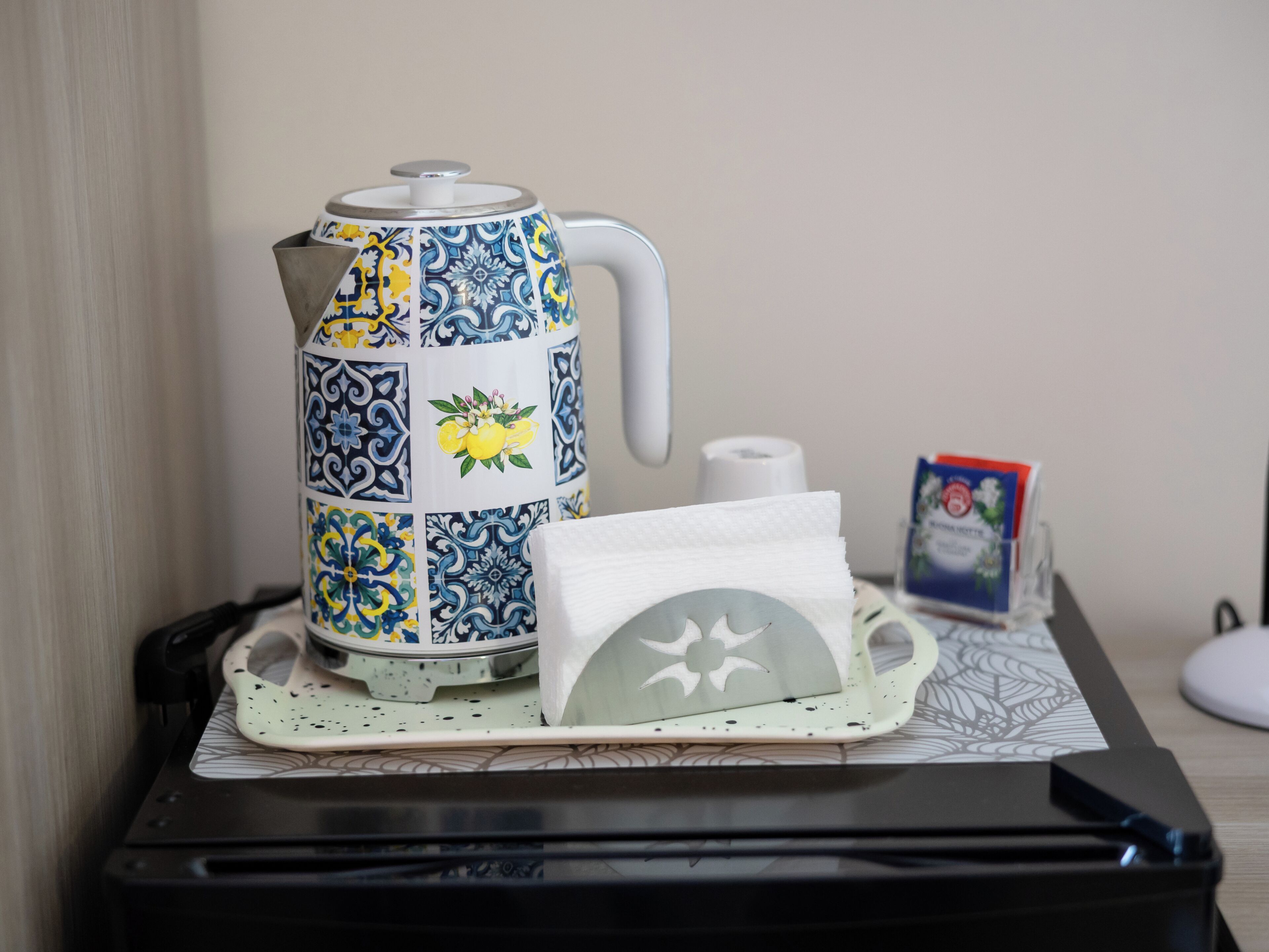 Une machine à café, des serviettes en papier et une boîte de mouchoirs sont posés sur une table recouverte d’un set de table à motifs.