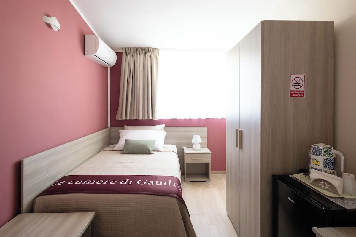 Ein Hotelzimmer mit Bett, Nachttisch, Kleiderschrank, Schreibtisch und einem Fenster mit Vorhängen.