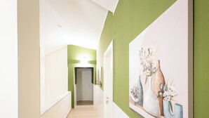 Un pasillo con pared verde, suelo de madera y un cuadro con jarrones a la derecha.