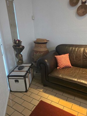 A living room with a brown leather sofa, a patterned cushion, a small table with a vase and a box, and a suitcase on the floor. - Sunny sanctuary in the heart of Gallo Manor (Sandton)