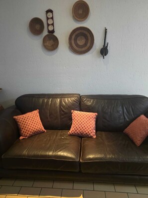 Ein braunes Ledersofa mit gemusterten Kissen, einer Wanduhr und dekorativen Tellern.