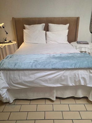 Ein ordentlich bezogenes Bett mit Kopfteil, ein Nachttisch mit Lampe und ein kleiner Tisch mit einem Buch.