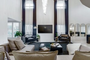 A modern living room with a large flat-screen TV, two leather armchairs, a sofa, and a coffee table.