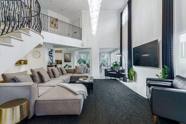 A spacious living area with a sectional sofa, a black leather armchair, a flat-screen TV, and a staircase with a decorative railing.