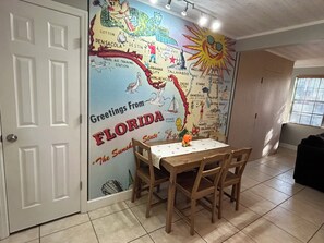 A dining area with a wall mural featuring Florida locations and a small table with chairs. - The Native-Vintage Florida Vibe in the Oldest City (St. Augustine)