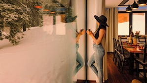 A person standing by a window with a snowy view, a dining area with chairs and a table, and a reflection of the person on the glass. - Mountain Chalet for 20 with Wellness, Sauna & Hot Tub — Ski-in/Ski-out (Martin)