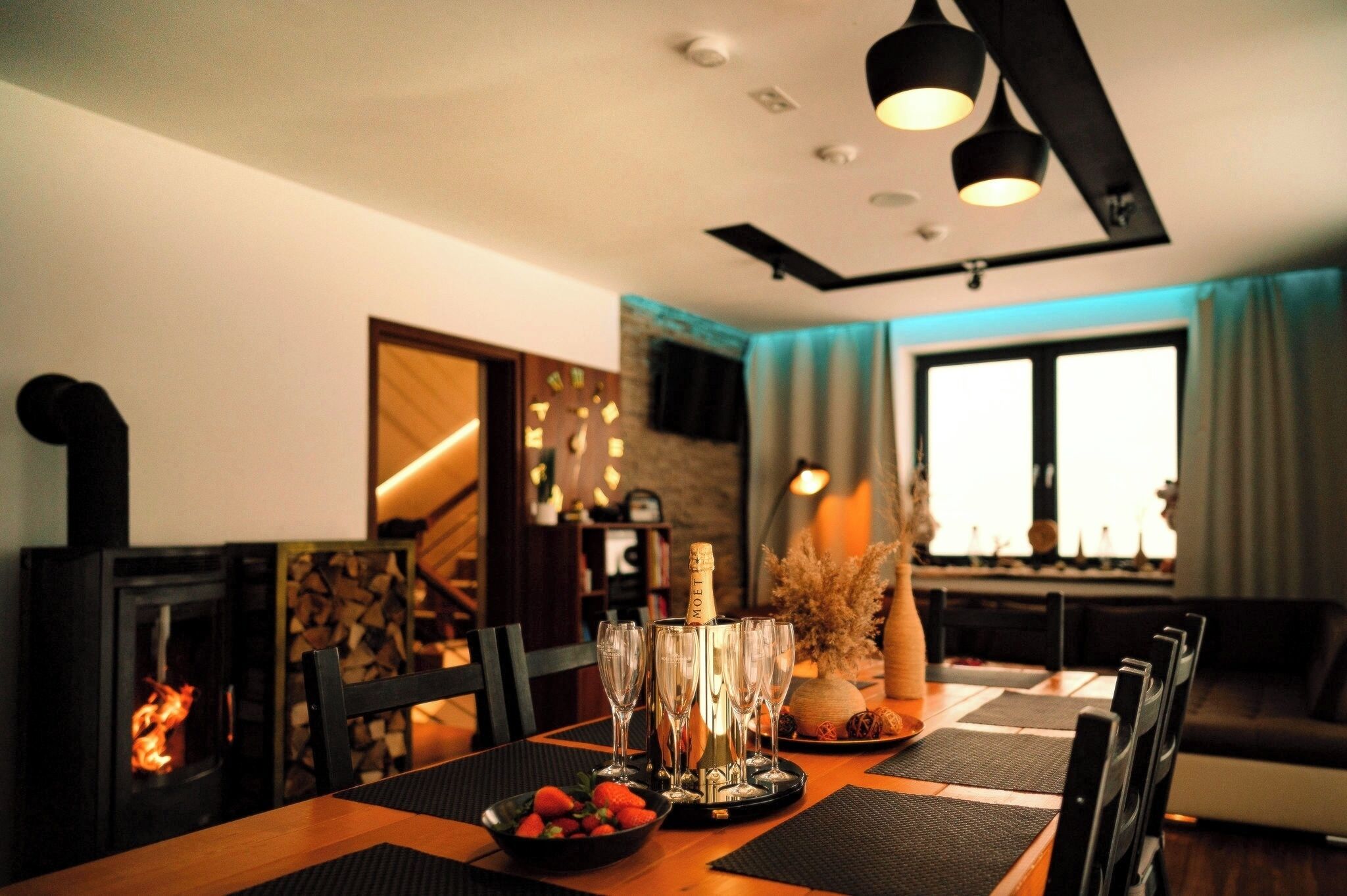 Un comedor con una mesa dispuesta para cuatro, una chimenea y una lámpara de techo moderna.