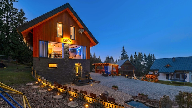 A modern wooden cabin with a stone foundation, a visible dining area, and a small outdoor deck. - Mountain Chalet for 20 with Wellness, Sauna & Hot Tub — Ski-in/Ski-out (Martin)