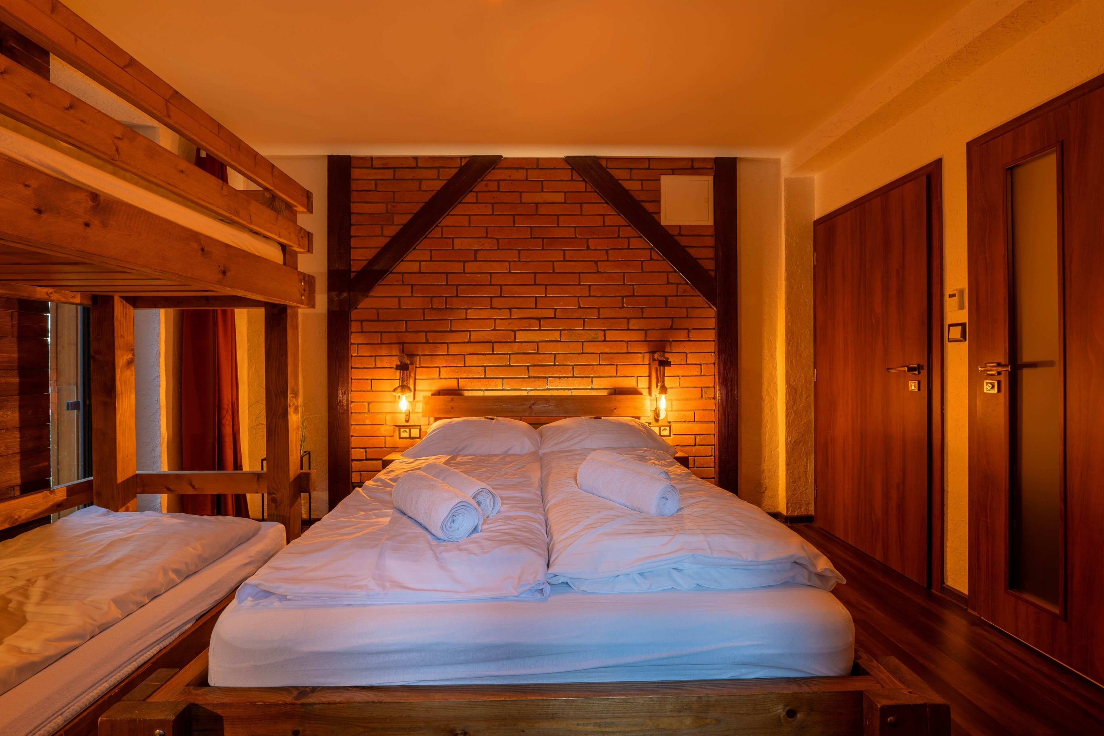 Een kamer met een houten bed, een houten bank en een bakstenen muur met een houten plafond.