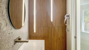 A bathroom with a wooden panel wall, a round mirror, a white sink, and a hairdryer. - Miramare Suites - Camera  Ardesia (Vasto)