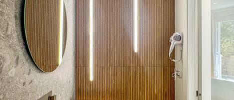 Un baño con pared de panel de madera, un espejo redondo, un lavabo blanco y un secador de pelo.