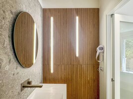 Un bagno con parete rivestita in legno, uno specchio tondo, un lavabo bianco e un asciugacapelli.