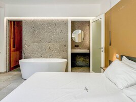Una camera da letto moderna con un letto grande, una vasca da bagno e un bagno con uno specchio e un lavandino.