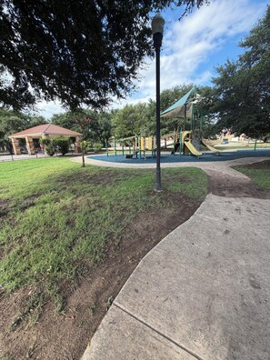 Um parque com um parquinho, um coreto e um caminho pavimentado.