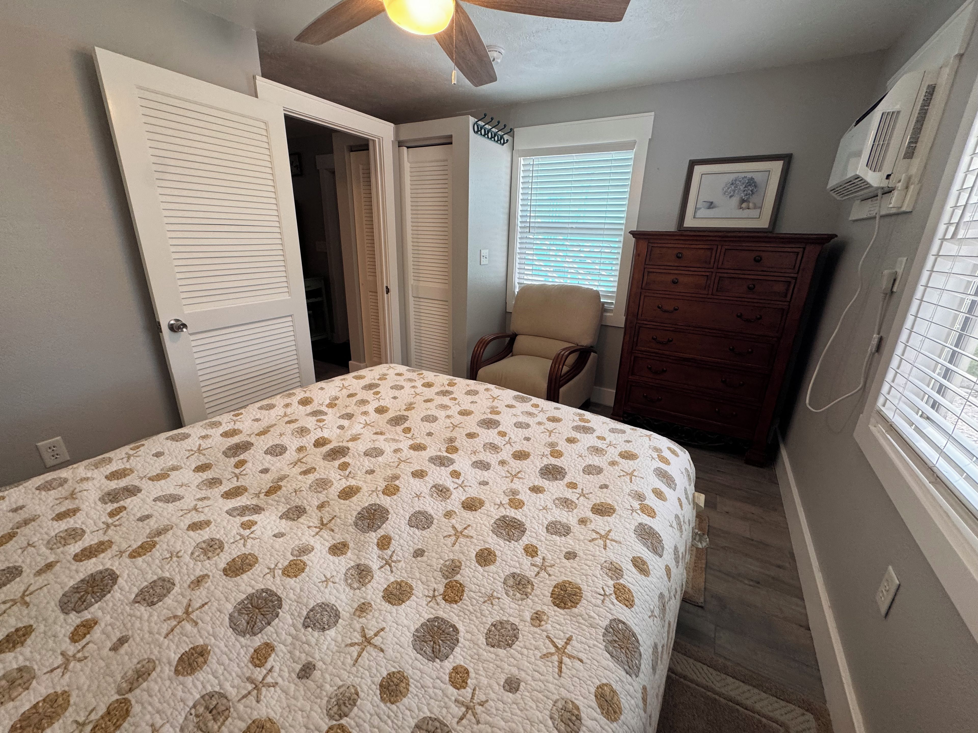 A bedroom with a bed, a chair, a dresser, and a ceiling fan.