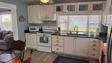 A kitchen with white cabinets, a microwave, an oven, a ceiling fan, and a window with blinds.