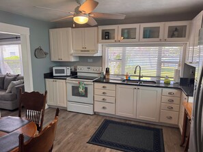 A kitchen with white cabinets, a microwave, an oven, a ceiling fan, and a window with blinds. - Malu Lani Cottage at Pirates Cove Inn & Marina - Boat Slip Included (Bokeelia)