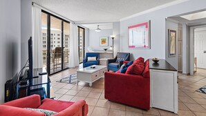 Ein Wohnzimmer mit einem roten Sofa, einem blauen Sessel, einem weißen Couchtisch und einem Fernseher.