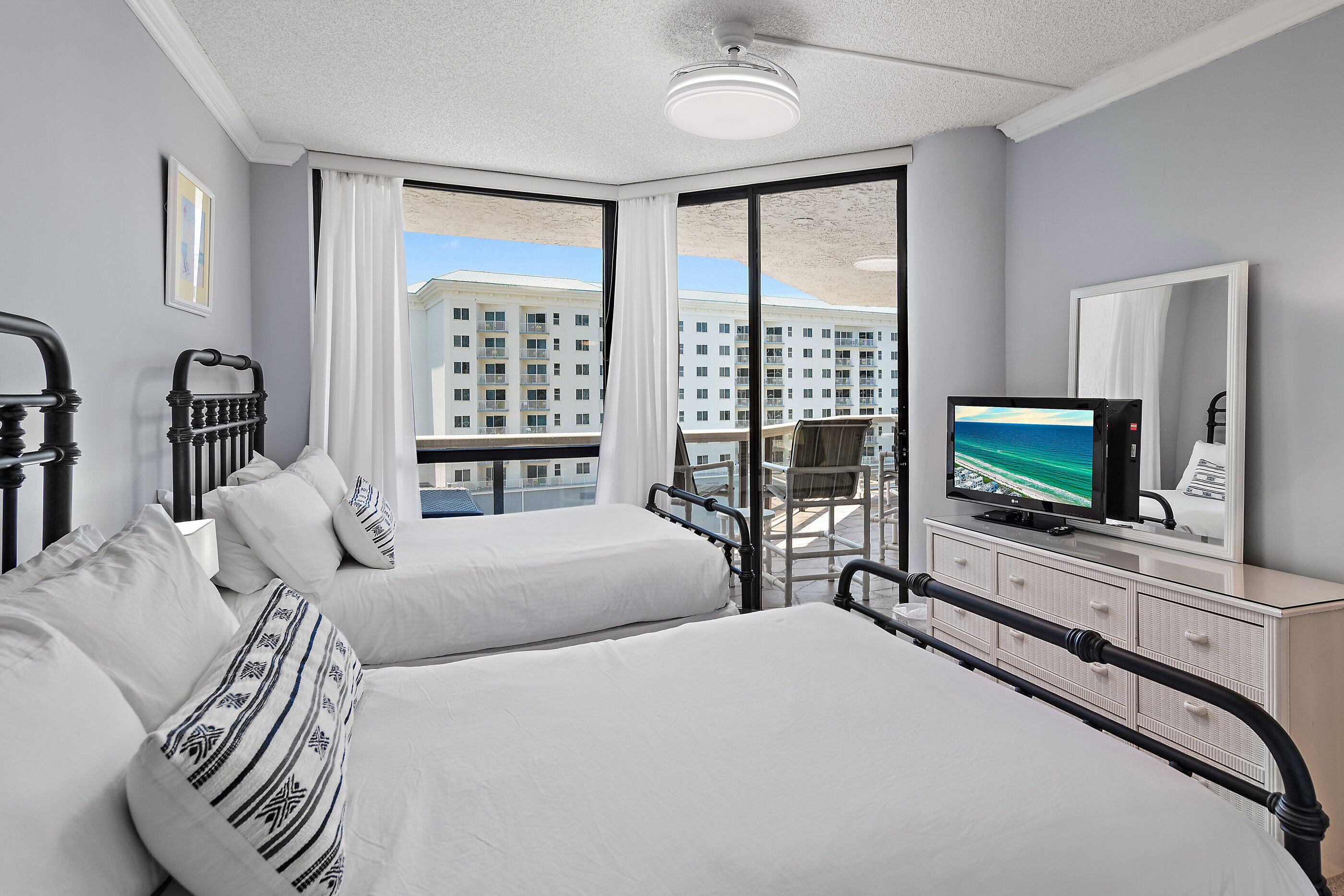 A hotel room with two beds, a television, a dresser, and a balcony with a view of a building.