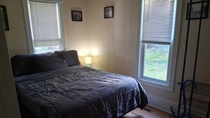Ein Schlafzimmer mit Bett, Nachttisch, Lampe und einem Fenster mit Jalousien.