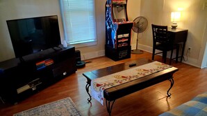 Ein Wohnzimmer mit Fernseher, Spielkonsole, Ventilator, Tisch und Stuhl.
