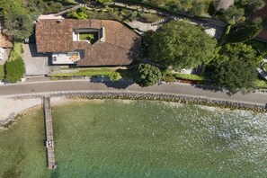 Eine Luftaufnahme eines Hauses mit Ziegeldach, einer an das Wasser gebauter Anlegestelle und einer Steinmauer, die das Grundstück umgibt.