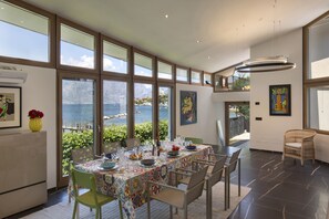 Ein Essbereich mit einem Tisch für vier Personen, großen Fenstern mit Meerblick und einer hohen Decke mit eingelassener Beleuchtung.