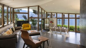 A spacious living area with a large window overlooking a scenic view, a dining area with a table set for two, and a comfortable seating arrangement. - Villa Locchi with private Pier (Malcesine)